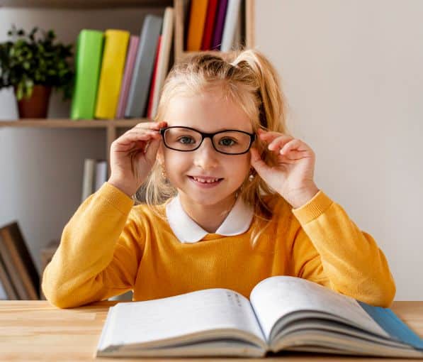 a young girl wearing myopia treatment glasses reading on a chair smiling