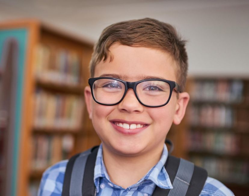 a smiling boy wearing myopia glasses with school backpack posing.