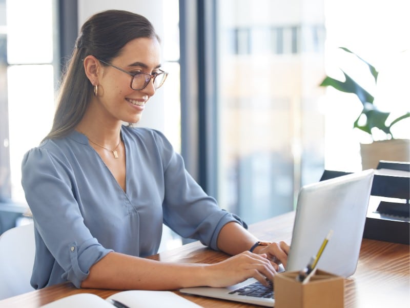 woman wearing blue light glasses sitting infront of computer.